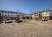 Thumbnail 29 of 33 - A parking lot in front of a multi-story apartment building with cars parked.