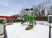 Thumbnail 30 of 53 - A playground with a green slide and a red building in the background.