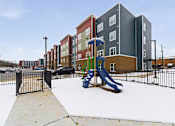 Thumbnail 23 of 53 - A playground with a slide and a fence in front of apartment buildings.