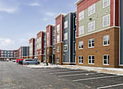 Thumbnail 46 of 53 - A row of multi-story apartment buildings with a parking lot in front.