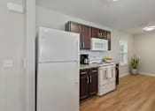 Thumbnail 31 of 31 - A white refrigerator stands in a kitchen with wooden cabinets and a white stove.