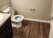 Thumbnail 42 of 49 - A white toilet with a blue bowl sits in a bathroom with wood flooring.