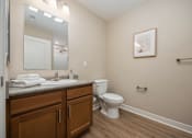 Thumbnail 47 of 48 - A bathroom with a toilet, sink, mirror, and wooden cabinets.
