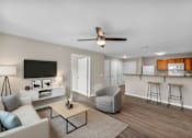 Thumbnail 52 of 54 - A living room with a white couch, a grey armchair, a wooden coffee table, and a flat-screen TV mounted on the wall.