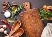 Thumbnail 3 of 3 - A wooden cutting board with a handle is surrounded by various herbs and spices.