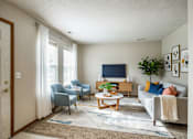 Thumbnail 18 of 19 - A living room with a grey couch, a blue chair, a wooden coffee table, and a flat screen TV.