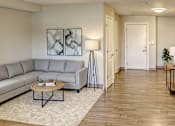 Thumbnail 25 of 25 - A living room with a grey sofa, a coffee table, and a painting on the wall.