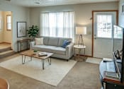 Thumbnail 15 of 17 - A living room with a grey couch, a coffee table, and a lamp.