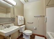 Thumbnail 21 of 24 - A white toilet sits in a small bathroom with a sink and mirror.
