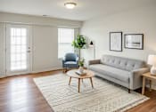 Thumbnail 26 of 28 - A living room with a grey couch, a blue chair, a coffee table, and a rug.