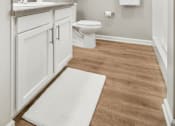 Thumbnail 25 of 26 - A white bathroom with a toilet, sink, and a rug on the floor.