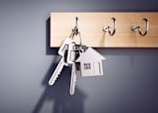 Thumbnail 1 of 3 - A set of keys is hanging from a hook on a wooden board, with a miniature house keychain attached to the keys.
