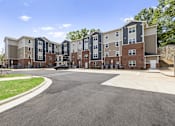 Thumbnail 24 of 31 - A large apartment complex with a parking lot in front.