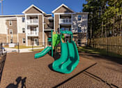 Thumbnail 12 of 55 - A playground with a green slide in front of apartment buildings.