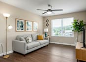 Thumbnail 45 of 45 - A living room with a grey couch, a floor lamp, a ceiling fan, and a wooden side table.