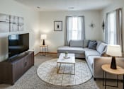 Thumbnail 26 of 28 - A living room with a grey couch, a television, and a coffee table.