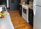 Thumbnail 38 of 39 - A kitchen with a white refrigerator, black cabinets, and a wooden floor.