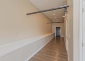 Thumbnail 34 of 39 - A long hallway with a white wall and a wooden floor.