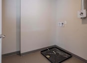 Thumbnail 22 of 39 - A room with a door, a wall-mounted speaker, and a black tray on the floor.
