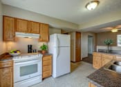 Thumbnail 25 of 28 - A kitchen with a white refrigerator, wooden cabinets, and a granite countertop.
