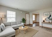 Thumbnail 27 of 28 - A living room with a grey sofa, a wooden coffee table, and a large painting on the wall.