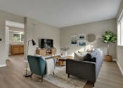 Thumbnail 9 of 9 - A living room with a grey couch, a green chair, a wooden cabinet, a TV, and a plant.