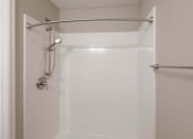 Thumbnail 27 of 29 - A white tiled shower with a glass door and a silver grab bar.
