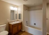 Thumbnail 58 of 78 - A bathroom with a white toilet, a wooden vanity with a sink, and a white bathtub.