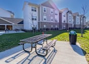 Thumbnail 48 of 56 - A park with a picnic table and bench in front of apartment buildings.