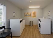Thumbnail 20 of 32 - A laundry room with a washer and dryer on each side and a chair in the middle.