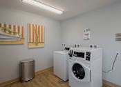 Thumbnail 23 of 32 - A laundry room with two washing machines and a trash can.