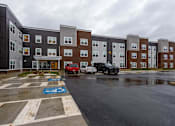 Thumbnail 29 of 37 - A parking lot in front of a building with cars parked.