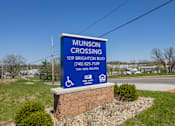 Thumbnail 24 of 32 - A blue sign for Munson Crossing is displayed in front of a grassy area.