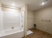 Thumbnail 10 of 24 - A white bathtub with a shower head and a white toilet in a bathroom.