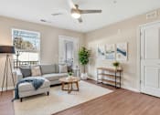 Thumbnail 51 of 51 - A living room with a grey sofa, a wooden coffee table, a white door, a white ceiling fan, and a white wall.