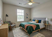 Thumbnail 27 of 28 - A bedroom with a bed, chair, and a ceiling fan.