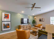 Thumbnail 30 of 30 - A living room with a television, orange armchair, and a green couch.