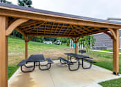 Thumbnail 20 of 30 - A wooden pergola with a black roof and two picnic tables.