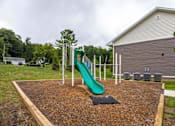 Thumbnail 21 of 30 - A playground with a green slide and a brown mulch area.