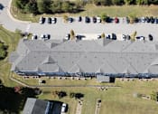 Thumbnail 20 of 52 - A large grey building with a grey roof and a parking lot in front.