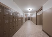 Thumbnail 51 of 58 - A long hallway with brown lockers on the left and a white door at the end.