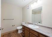 Thumbnail 41 of 58 - A bathroom with a toilet, sink, mirror, and a wooden floor.