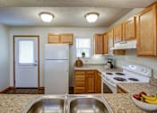 Thumbnail 32 of 34 - A kitchen with a white refrigerator, wooden cabinets, and a bowl of fruit on the counter.