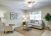 Thumbnail 27 of 28 - A living room with a beige couch, a coffee table, a lamp, and a plant.