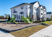 Thumbnail 41 of 55 - A playground with a green slide in front of a white apartment building.