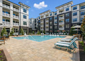 Thumbnail 10 of 20 - A swimming pool surrounded by sun loungers and apartment buildings.