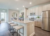 Thumbnail 1 of 28 - one bedroom kitchen with gooseneck black faucet on the island,  woodgrain light cabinets, stainless steel appliances, granite countertops, kitchen table with blue leather chairs, 6-panel white doors, woodlike plank flooring, and laundry room off the kitchen
