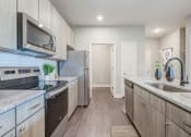 Thumbnail 4 of 28 - one bedroom kitchen with gooseneck black faucet on the island,  woodgrain light cabinets, stainless steel appliances, granite countertops, kitchen table with blue leather chairs, 6-panel white doors, woodlike plank flooring, and laundry room off the kitchen