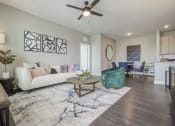Thumbnail 2 of 28 - living room with wood-like plank flooring, large rug and ceiling fan, white couch and light throw pillows.  View of kitchen and bar with recessed lighting and kitchen table, round with blue leather chairs