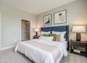 Thumbnail 8 of 28 - bedroom with plush carpet, white trim and taupe walls, bed with blue velvet headboard and two lamps on either side nightstand, walk-in closet and entry to the bathroom